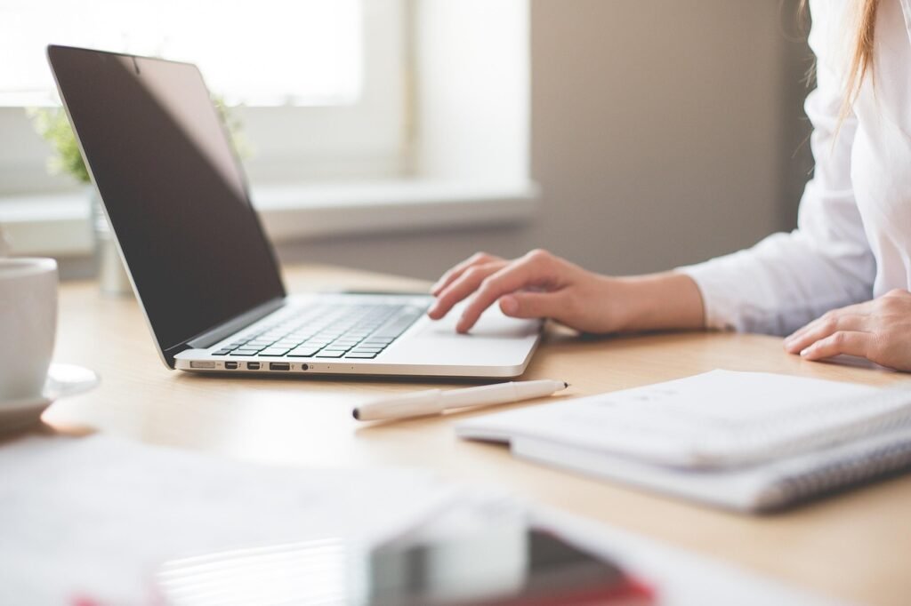 A professional content creator using a laptop to compare AI writing tools at a sunlit wooden desk with a notebook and coffee.