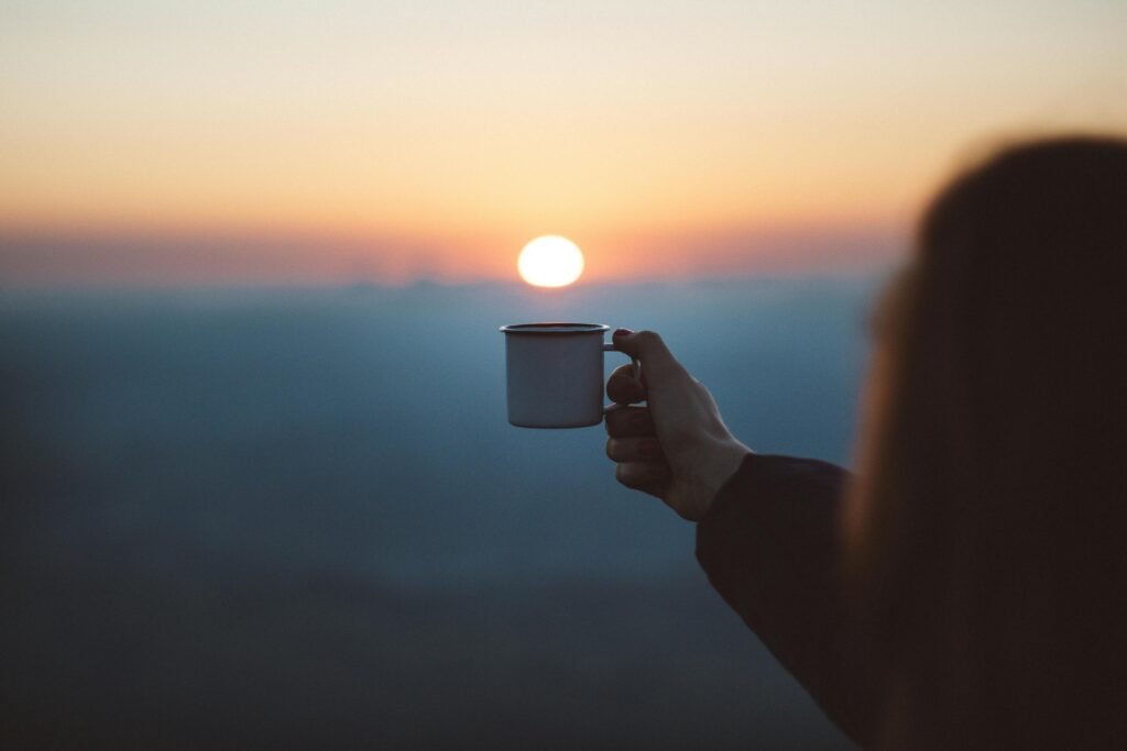 A person holding a coffee mug toward a sunrise over a vast horizon, symbolizing human judgment and original intention in an era of automated AI writing.