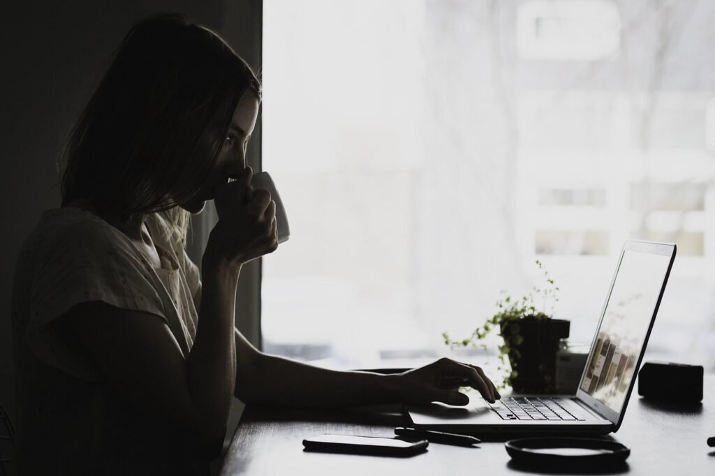 Person writing on a laptop at a desk with natural light, representing focused academic work.