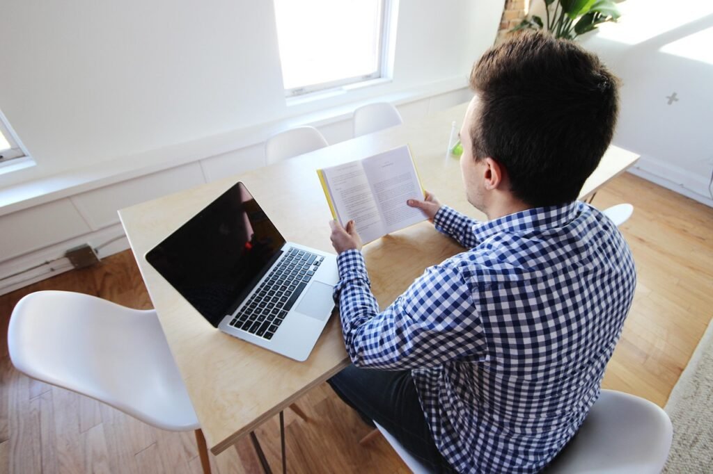 Student reading notes at a desk with laptop while writing an academic paper using AI writing tools.