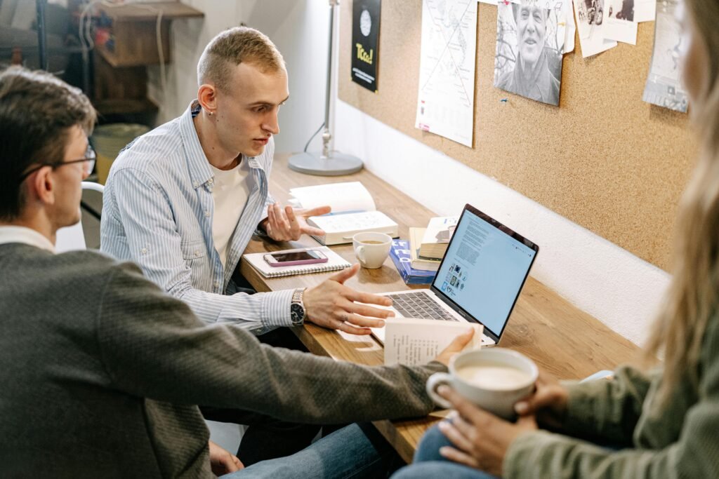 A group of people collaborating around a laptop and an open book, discussing information together in a study workspace, representing the DeepL vs Google Translate comparison.