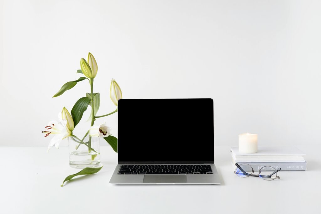 Elegant minimalist desk setup with laptop, white lilies, books, and candle.