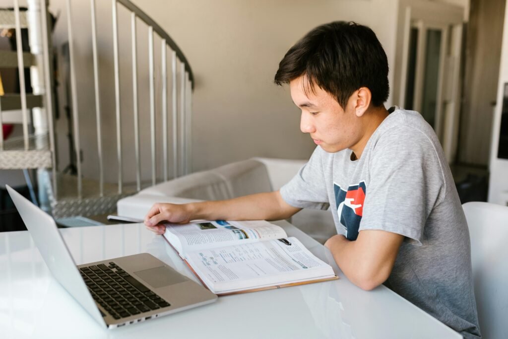 Master's student studying at home with laptop and textbook for postgraduate dissertation writing.