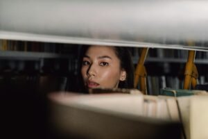 Researcher peering through library bookshelf surrounded by books contemplating originality and knowledge in the age of AI.
