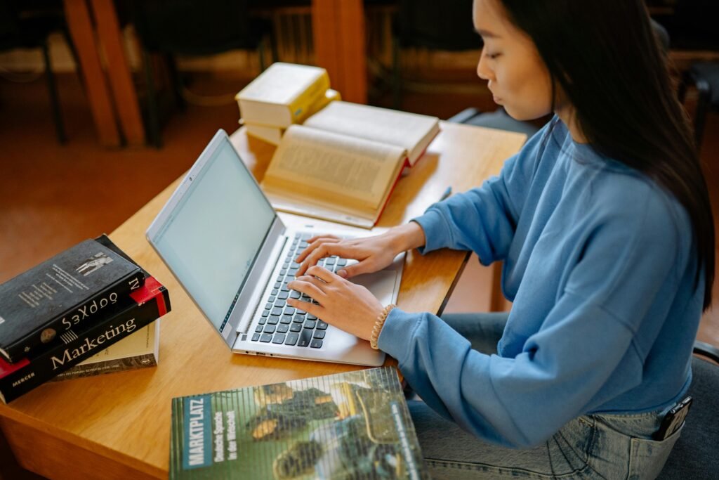 Researcher writing academic paper on laptop surrounded by books and study materials.